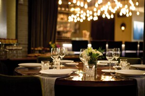 A restaurant table set with plates, glasses, and cutlery, with a decorative vase of flowers in the center. - Archer Hotel New York (New York)