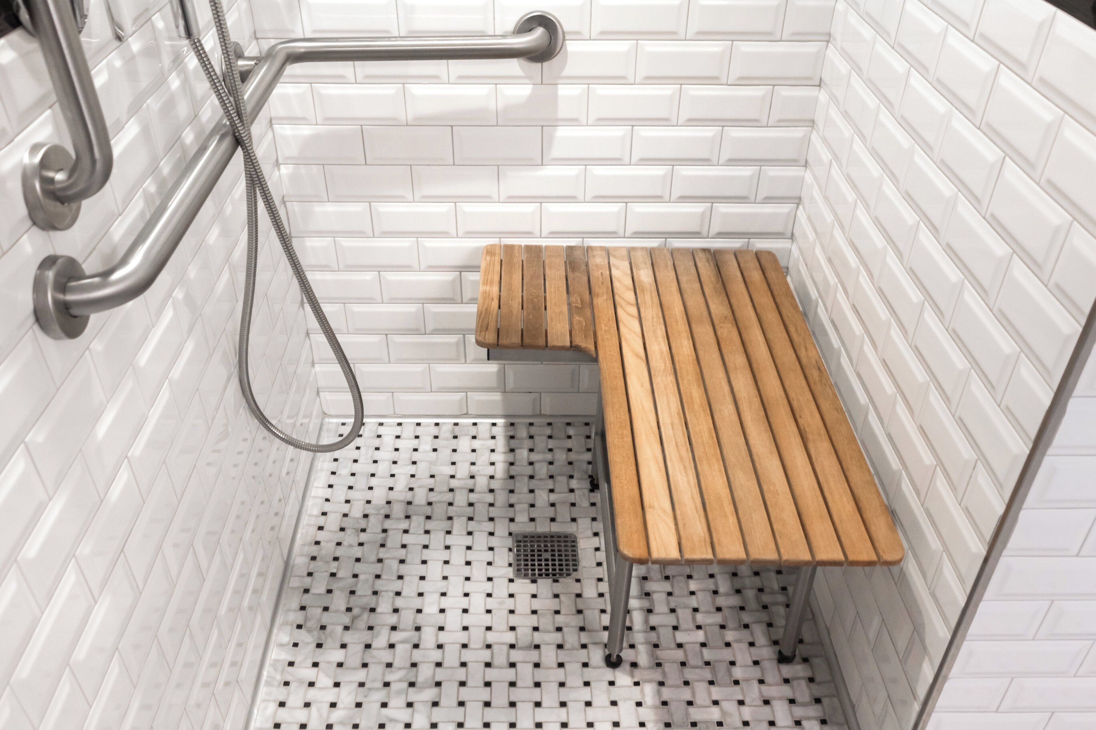 A shower area with white tiled walls, a wooden bench, and a handheld showerhead.