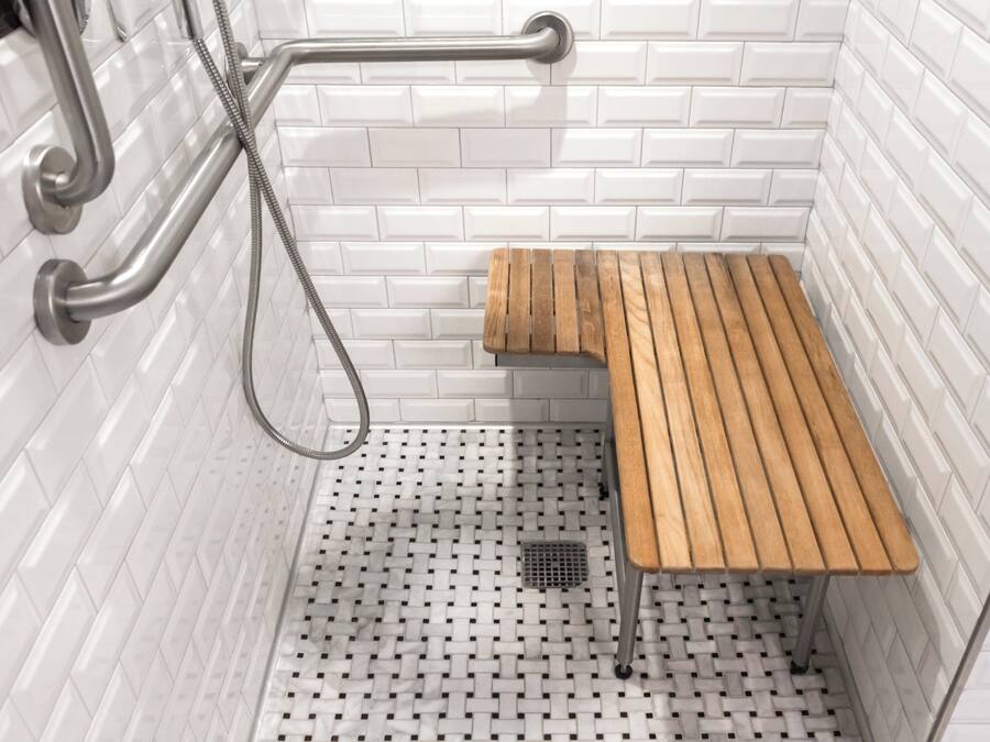 A shower area with white tiled walls, a wooden bench, and a handheld showerhead.