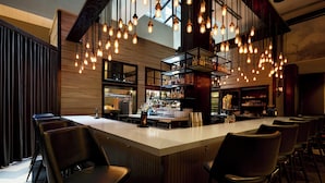 A bar area with a long counter, multiple hanging light fixtures, and several bar stools. - Archer Hotel New York (New York)