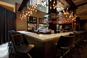 Un espace bar doté d’un long comptoir, de plusieurs luminaires suspendus et de plusieurs tabourets de bar.