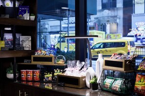 Interior de una tienda con estantes llenos de libros, aperitivos y agua embotellada.