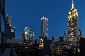A cityscape at dusk with illuminated skyscrapers, including a prominent building with a spire. - Archer Hotel New York (New York)