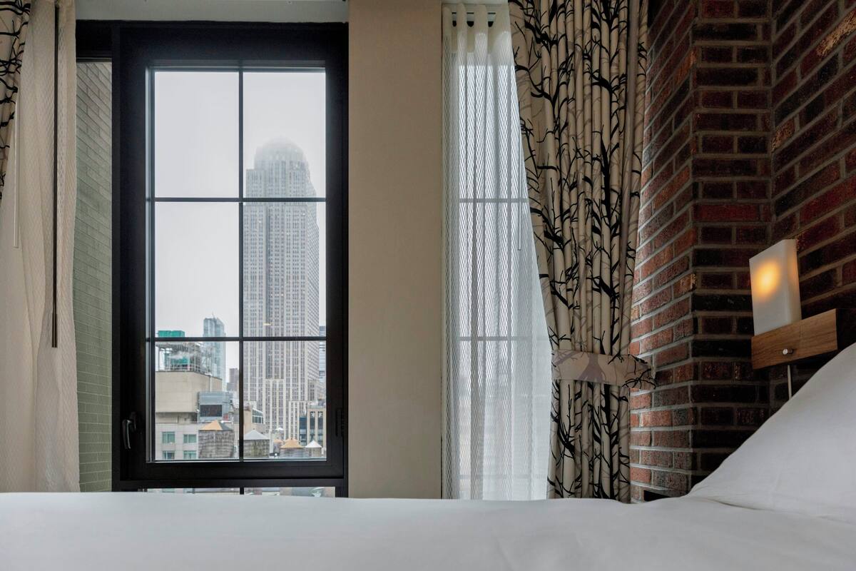 A hotel room with a large window, a bed, a nightstand, and a lamp.