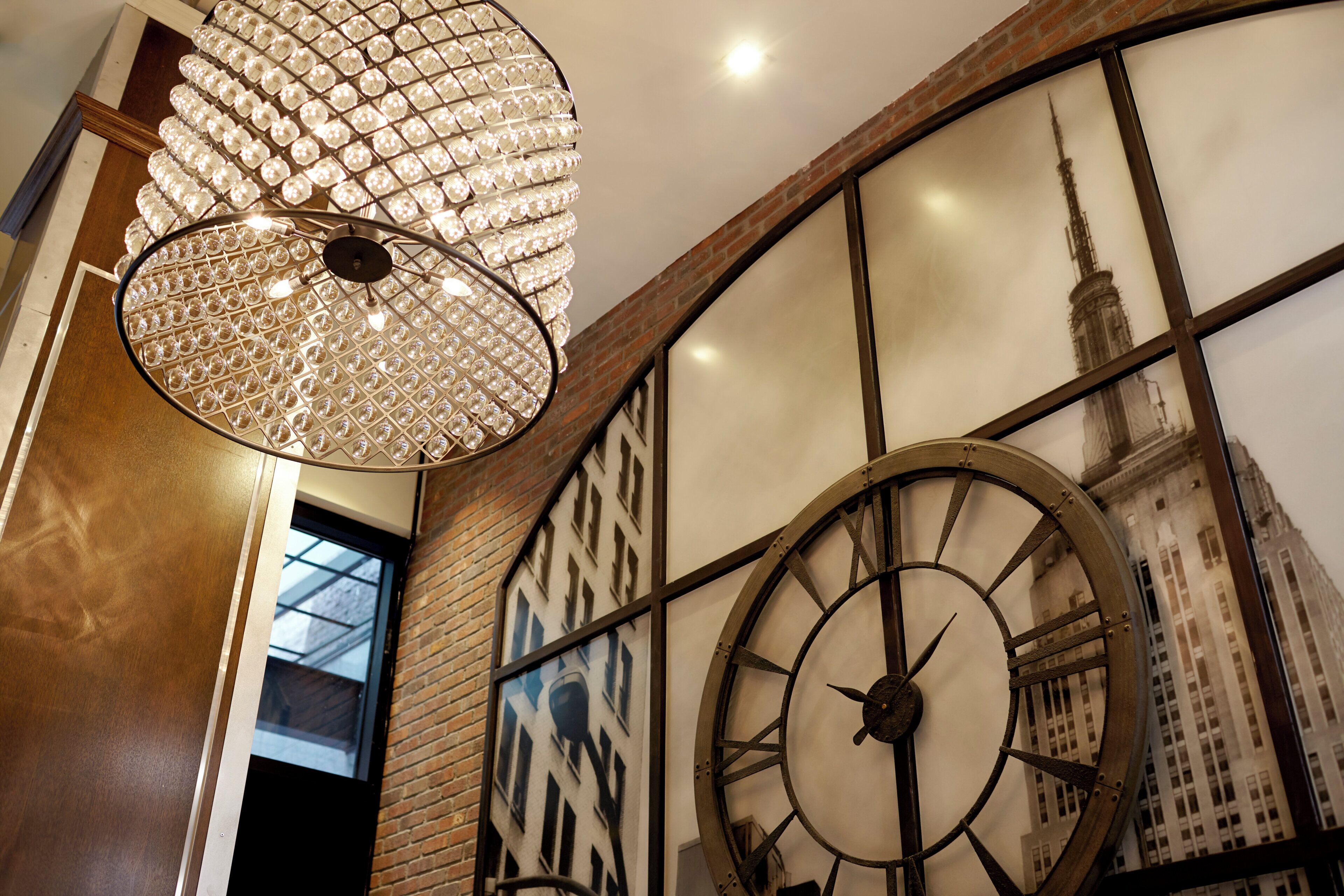 Un interno moderno con un'ampia lampada a pendente decorata, un orologio da parete ornamentale e vista sulla città attraverso una finestra.