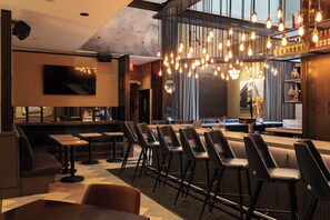 Uma área de bar moderna com várias opções de assento, incluindo banquetas e um sofá, e uma televisão fixada na parede.