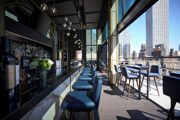 Un bar con una barra larga, taburetes azules y vistas a la ciudad.