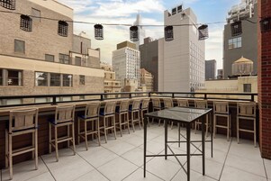 Een terras op het dak met een tafel en stoelen, met uitzicht op een stadslandschap met moderne gebouwen.