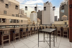 Une terrasse sur le toit, avec une table et des chaises, d’où l’on peut admirer un panorama sur la ville, avec ses bâtiments modernes.