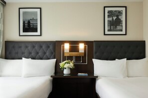 Quarto de hotel com duas camas, mesa de cabeceira com um vaso de flores e quadros nas paredes.