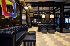 Un área de estar moderna con un sofá de cuero negro, un reposapiés a rayas y una zona de bar con pared de ladrillo y estanterías para vino.