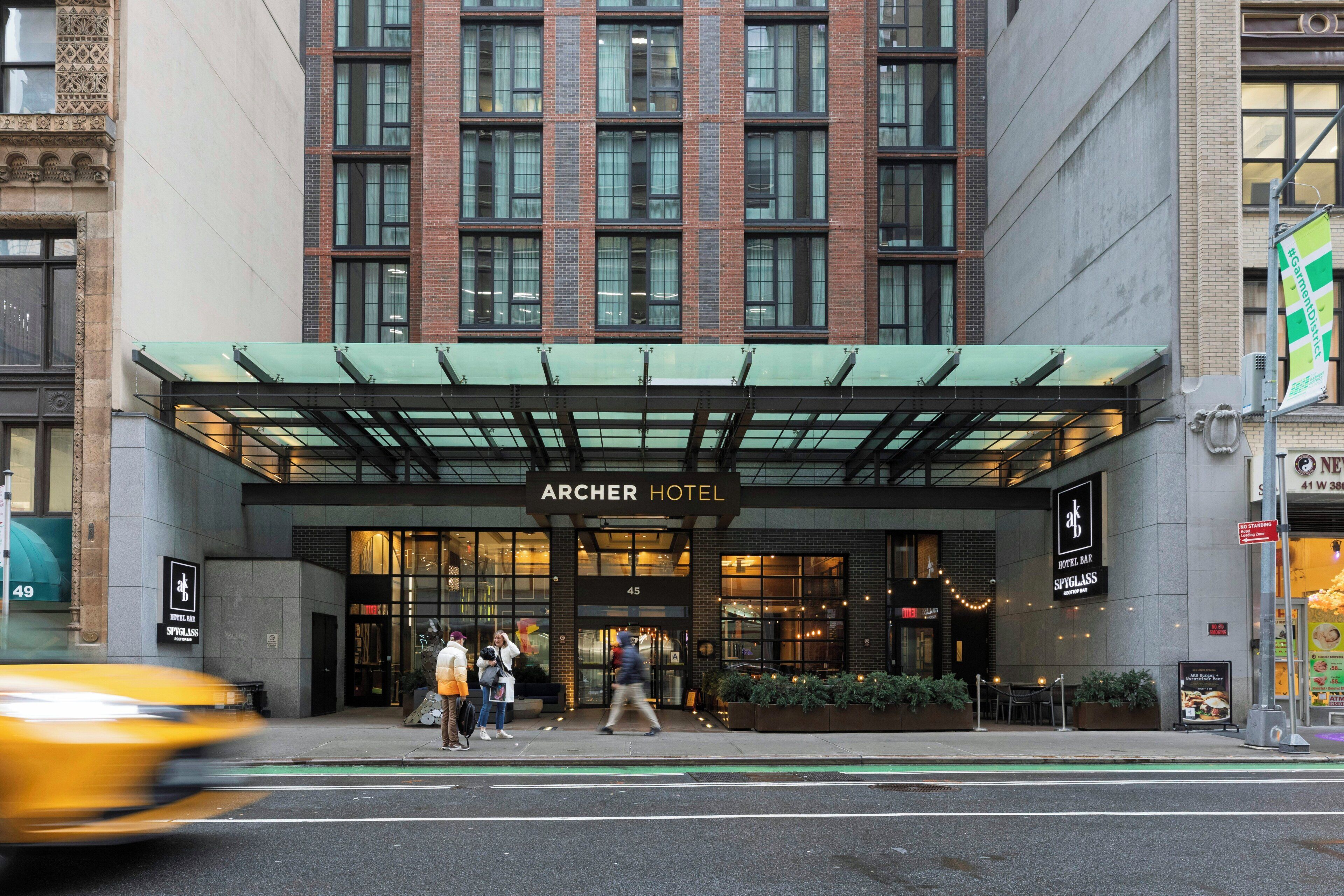 The Archer Hotel entrance with a modern facade, large windows, and a green awning.