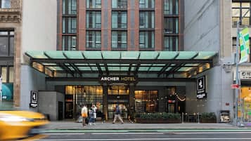 The Archer Hotel entrance with a modern facade, large windows, and a green awning.