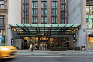 The Archer Hotel entrance with a modern facade, large windows, and a green awning. - Archer Hotel New York (New York)