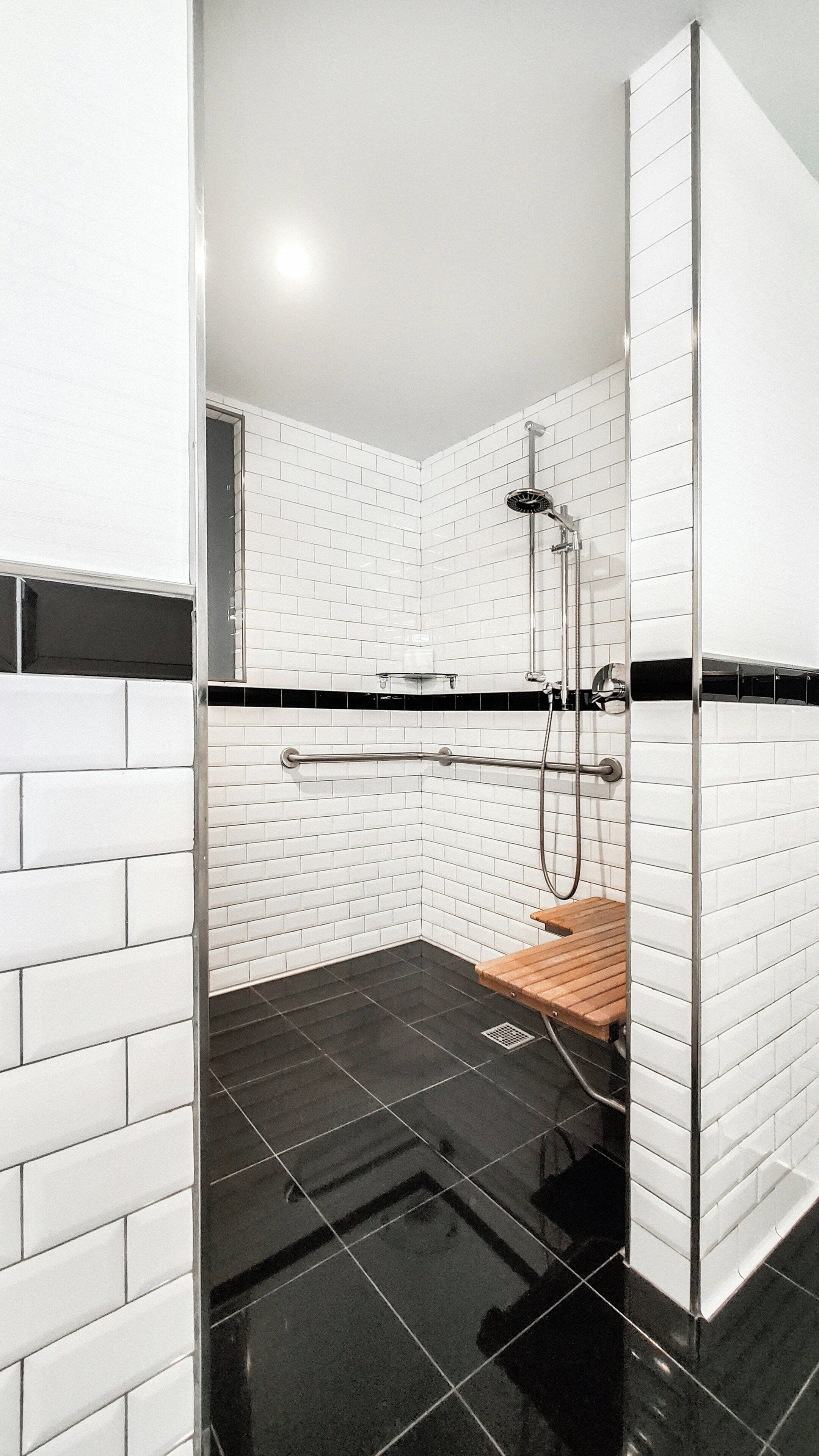 Un espace douche moderne avec des murs recouverts de carreaux blancs, un sol noir et un banc en bois.