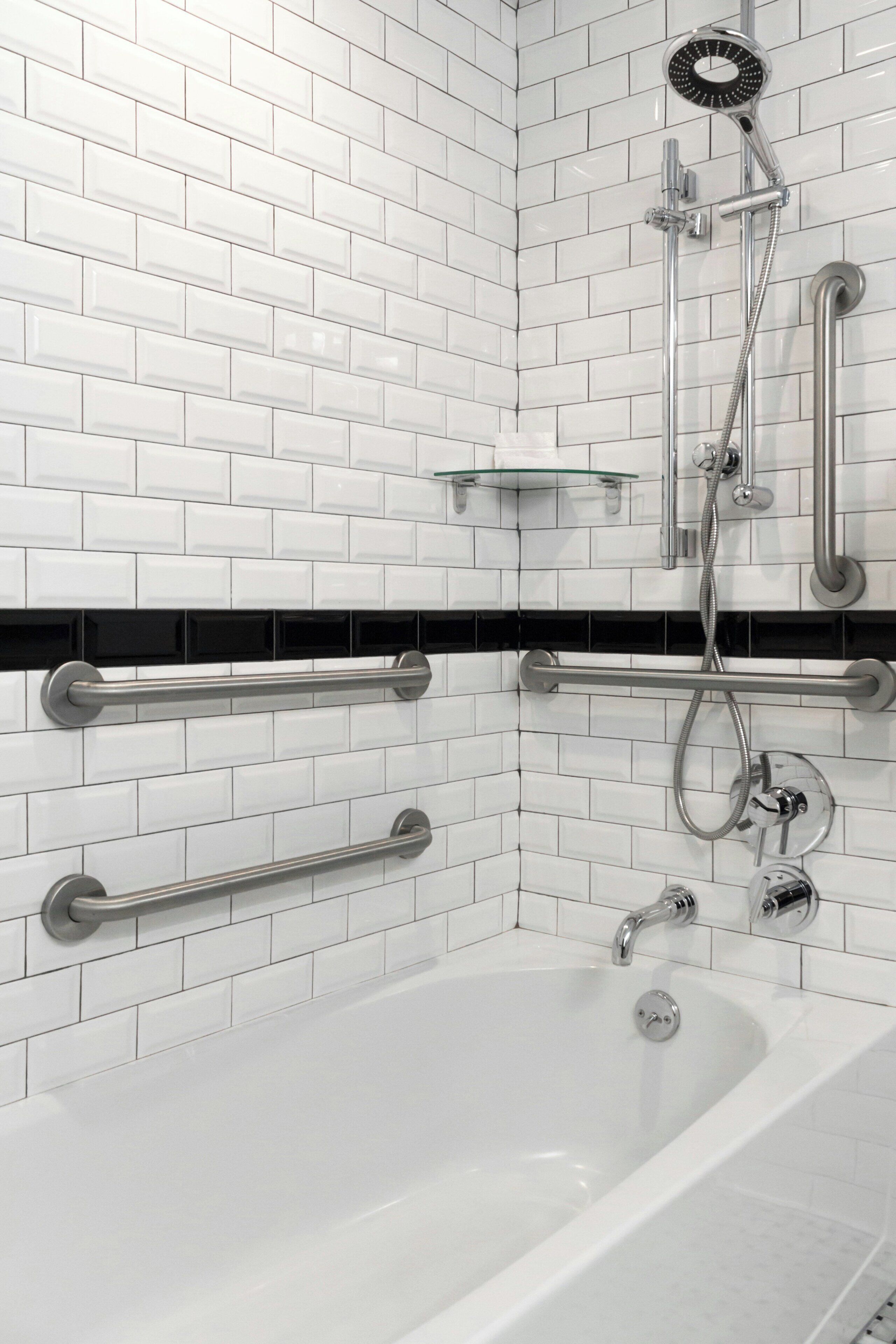 Ein modernes Badezimmer mit weißen Fliesen im U-Bahn-Stil, einer weißen Badewanne und einer Handbrause.
