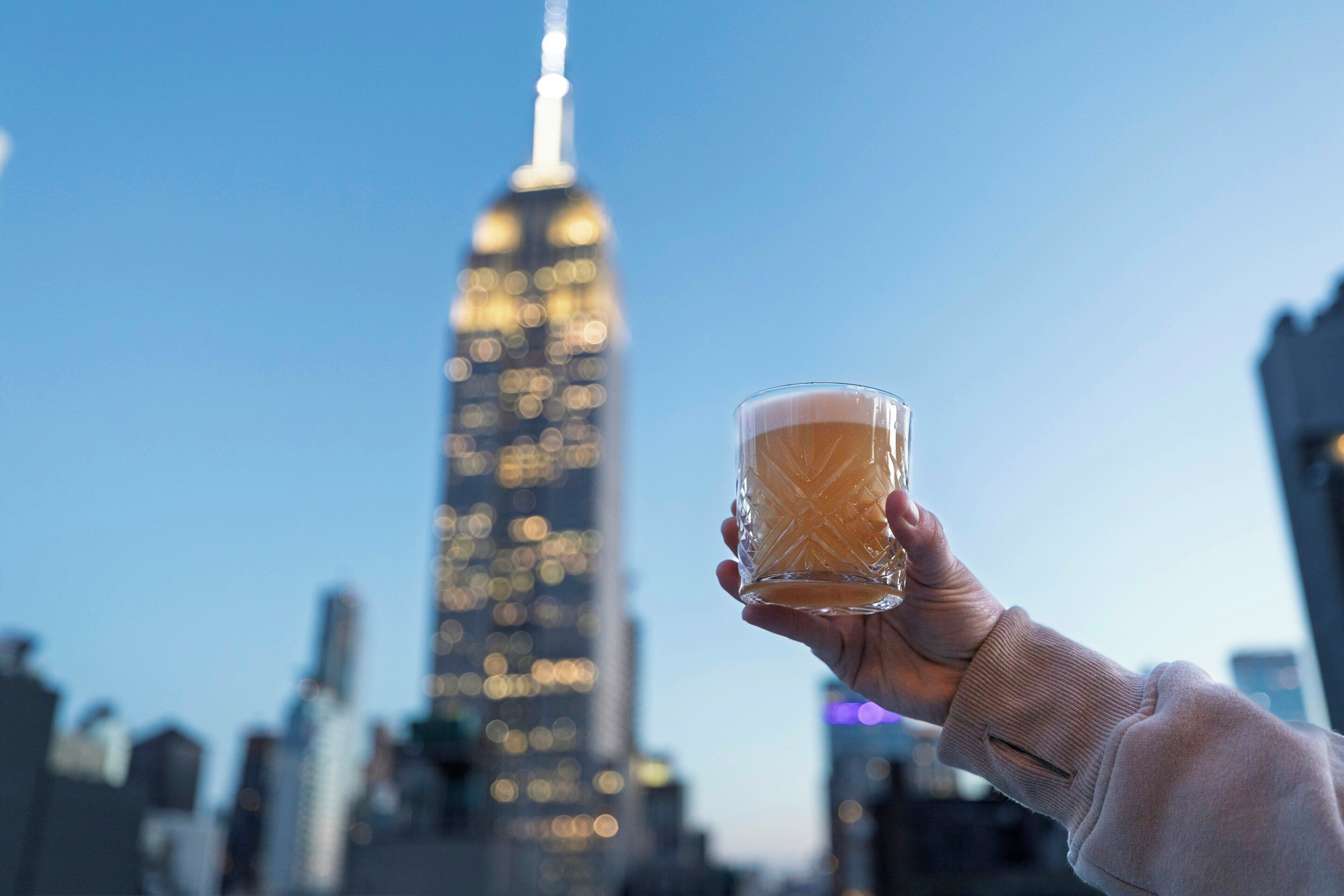 A hand holding a glass with a cityscape in the background.