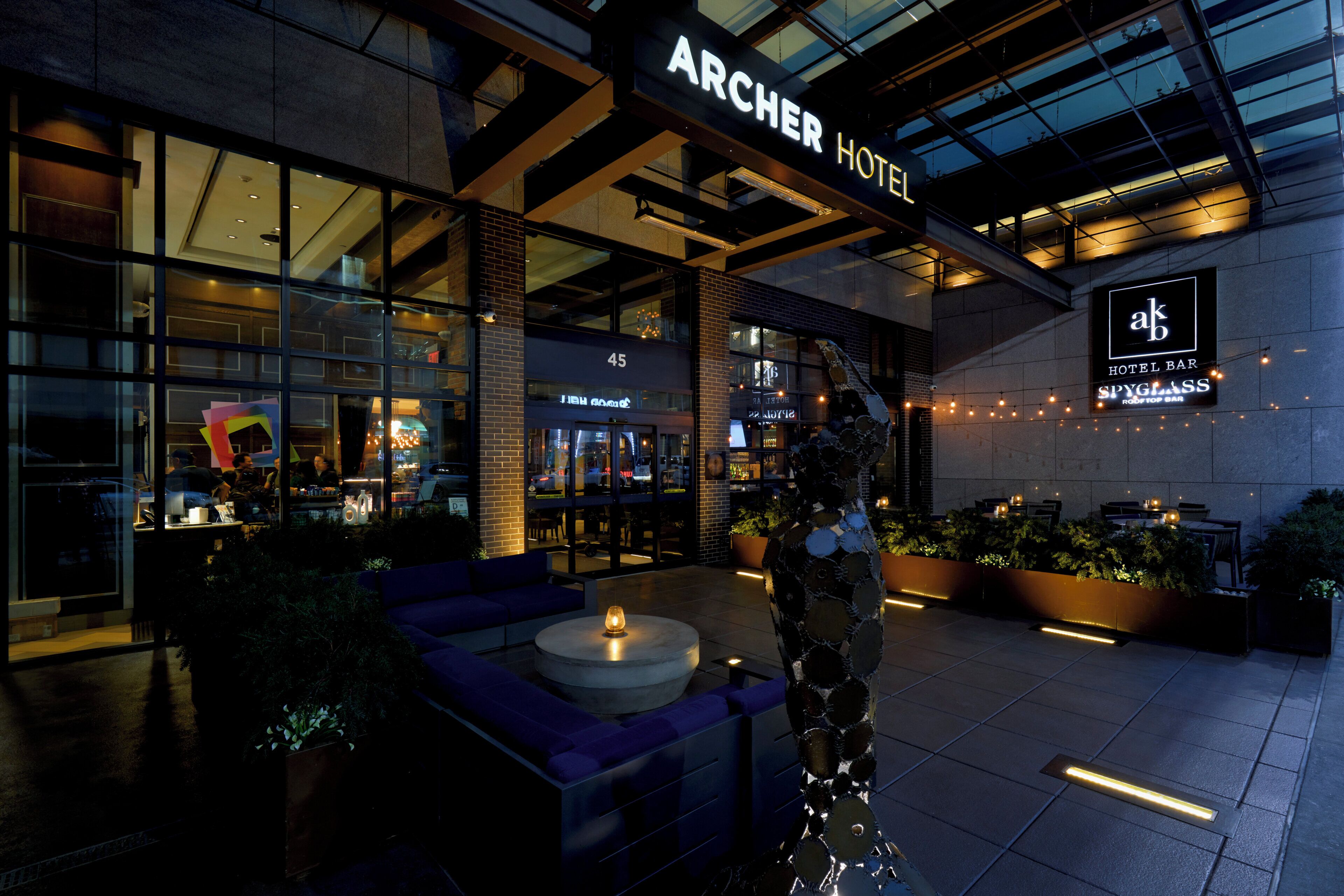 L’hôtel Archer présente une façade au design moderne, un espace extérieur aménagé avec des sièges et un restaurant bien visible appelé « Spyglass ».