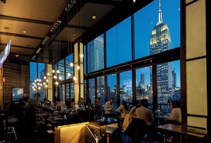A restaurant with large windows offering a view of the Empire State Building. - Archer Hotel New York (New York)