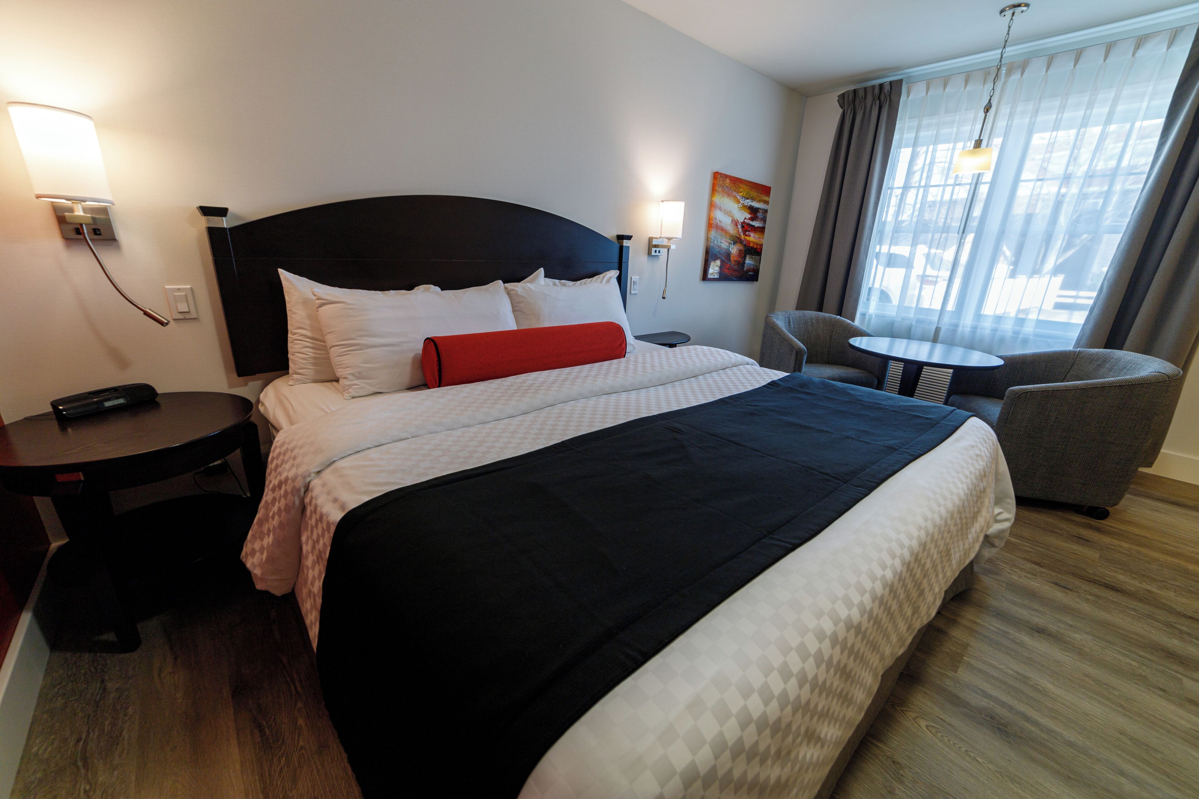Habitación de hotel con una cama grande, mesitas de noche, una silla, una pequeña mesa y vistas al exterior a través de la ventana.
