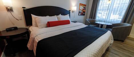 Et hotelværelse med en stor seng, sengeborde, en stol, et lille bord og udsigt til det fri gennem vinduet.
