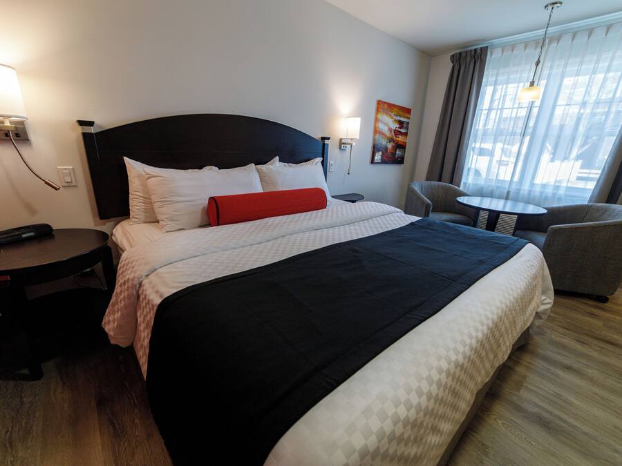 Habitación de hotel con una cama grande, mesitas de noche, una silla, una pequeña mesa y vistas al exterior a través de la ventana.