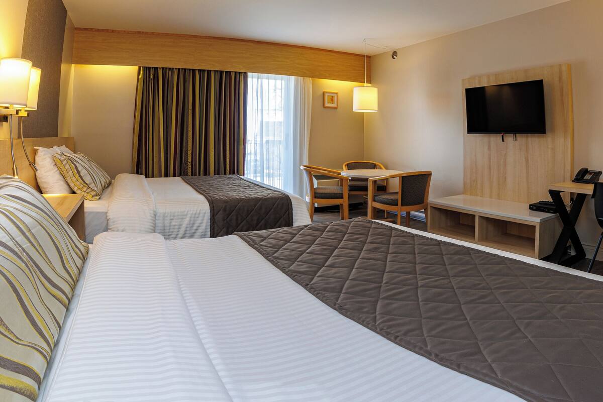 Ein Hotelzimmer mit zwei Betten, einem Schreibtisch, einem Sessel, einem Fernseher und einem Fenster mit Vorhängen.