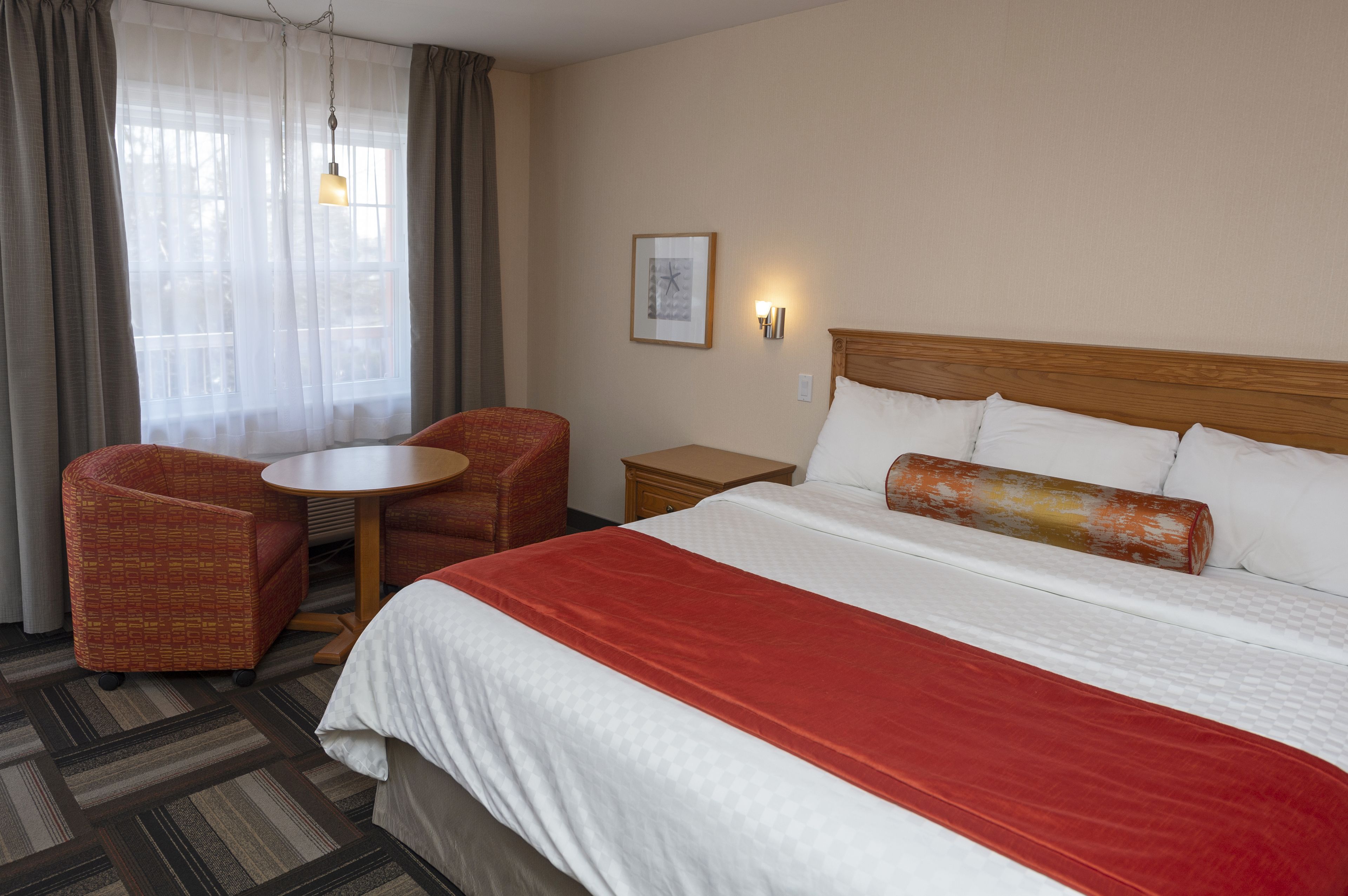A hotel room with a large bed, two chairs, a small table, and a nightstand.