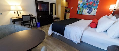 A hotel room with a bed, a desk, a television, and a painting on the wall.