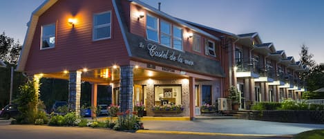 A hotel with a red facade, a sign reading "Le Castel de la mer," and a welcoming entrance with outdoor seating.