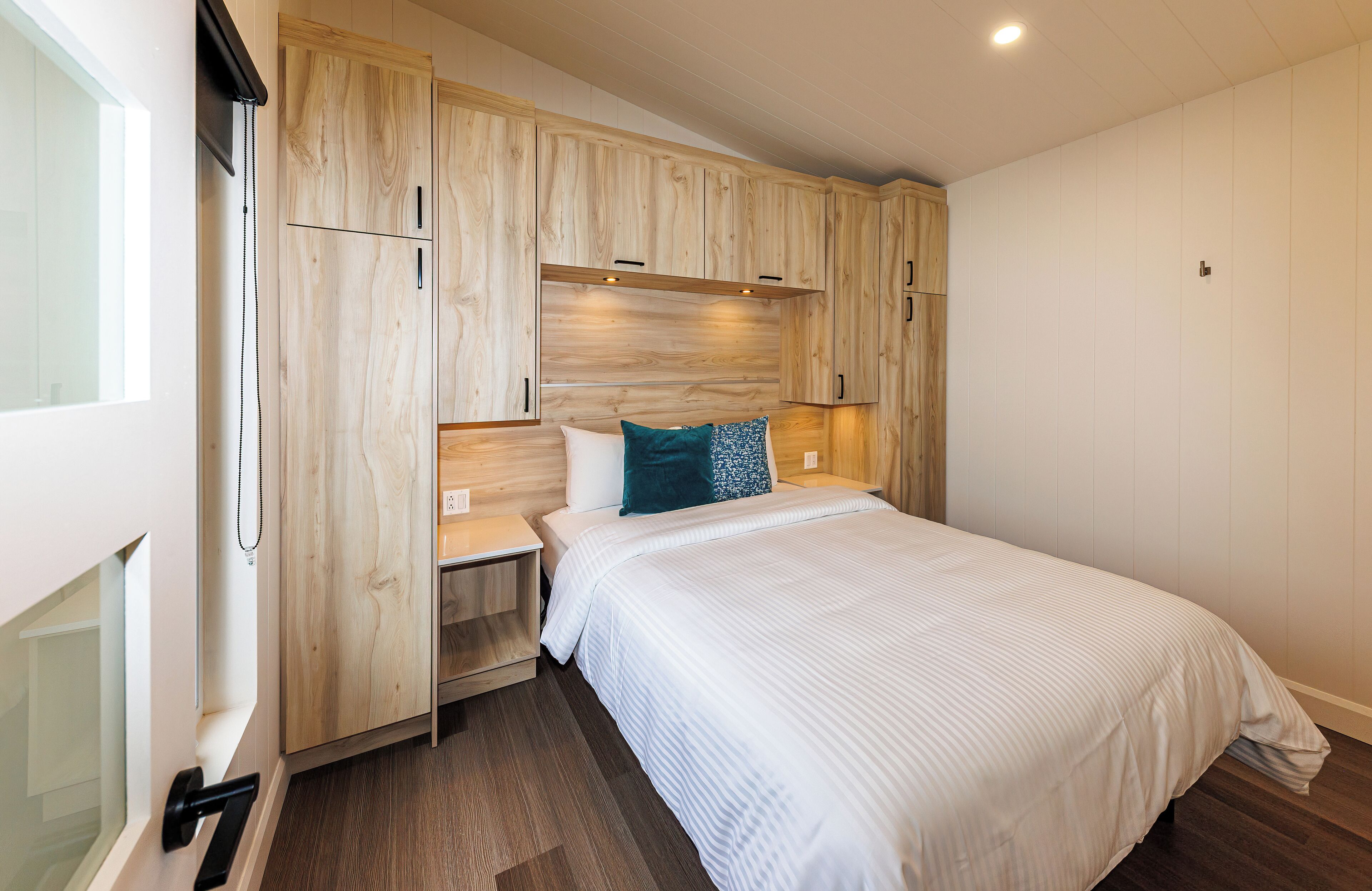 Quarto com cama, guarda-roupa de madeira, mesa de cabeceira e janela.