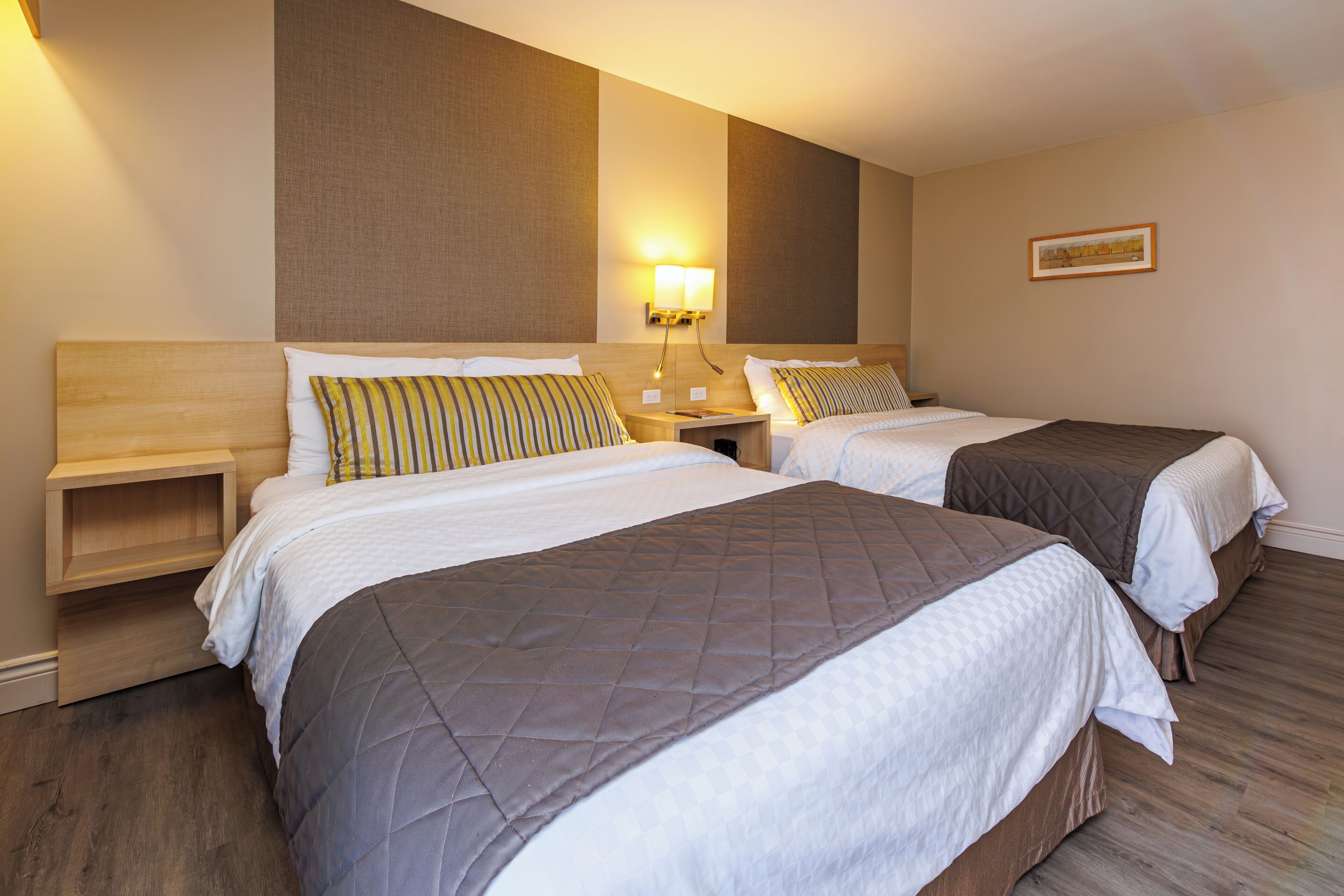A hotel room with two beds, wooden headboards, and bedside tables with lamps.