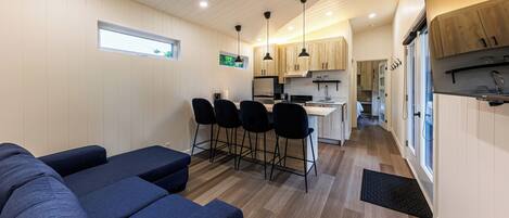 A compact living space with a kitchenette, a dining area with bar stools, and a seating area with sofas.