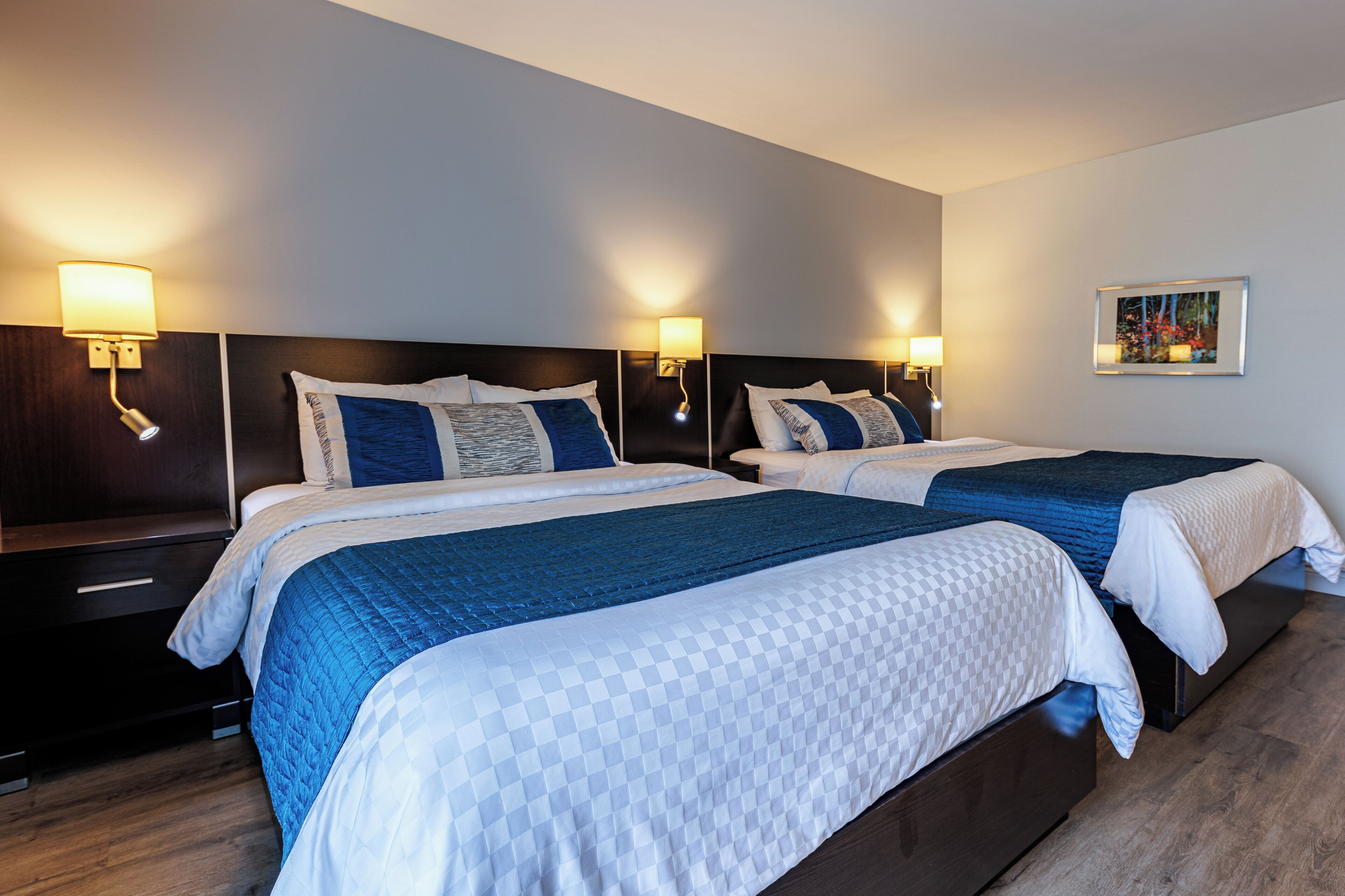 A hotel room with two beds, each with a headboard, bedside tables, and wall-mounted lamps.