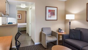 Ein Hotelzimmer mit einem Bett, einem Schreibtisch mit Stuhl, einer Couch, einem kleinen Tisch mit Lampe und einem gerahmten Bild an der Wand.
