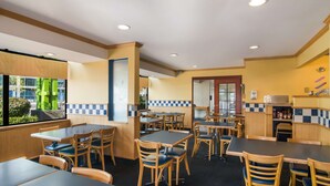 Ein Restaurant mit mehreren Tischen und Stühlen, einem Küchenbereich und Blick auf Grünflächen.
