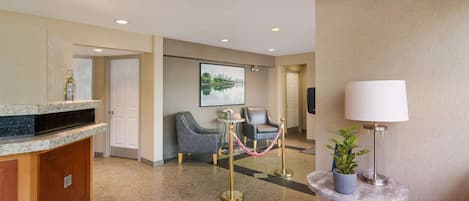 Un vestíbulo de hotel con mostrador de recepción, zona de estar y un cuadro con una vista urbana enmarcada en la pared.