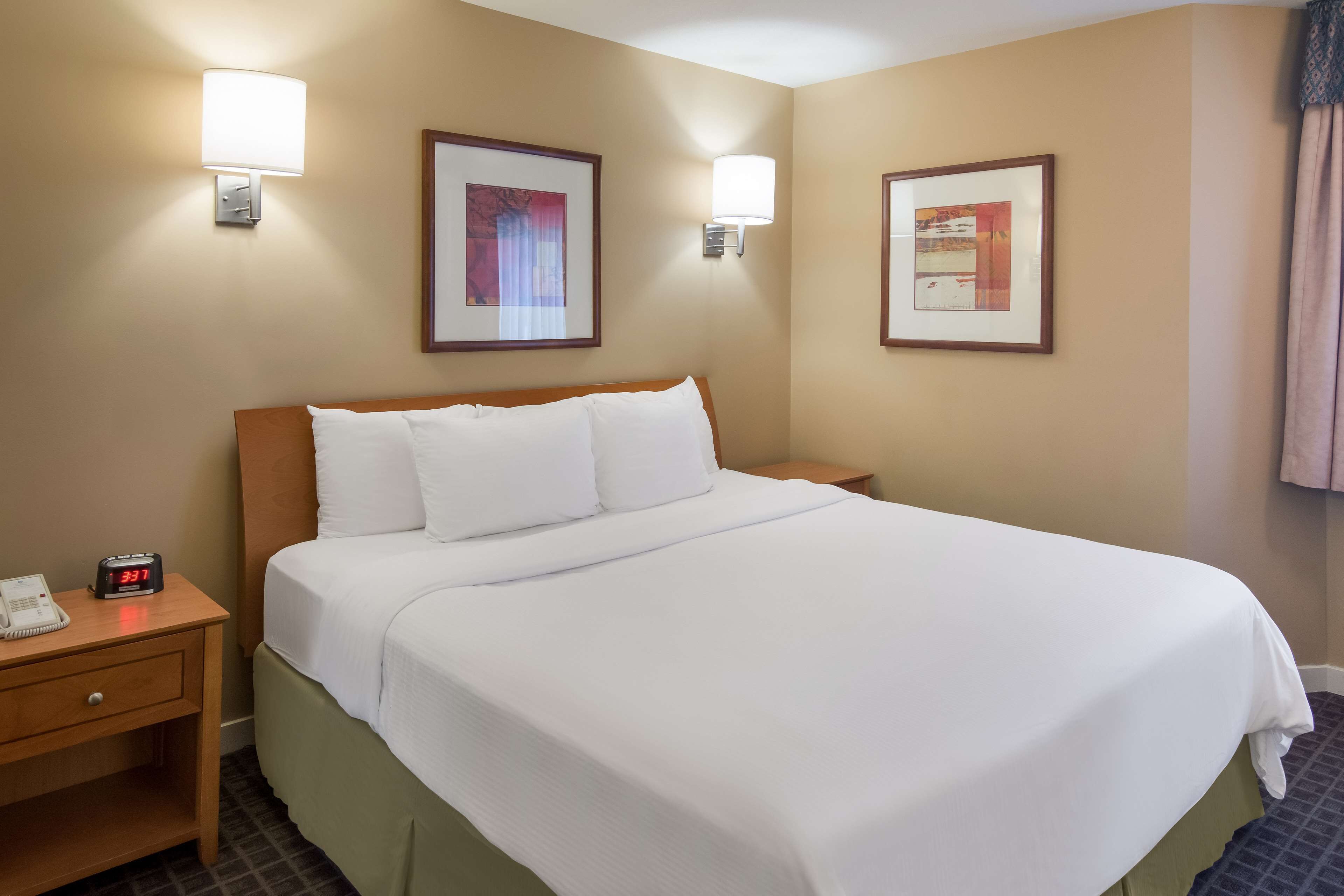 A hotel room with a large bed, two bedside tables, a nightstand, a clock, and two wall-mounted lamps.