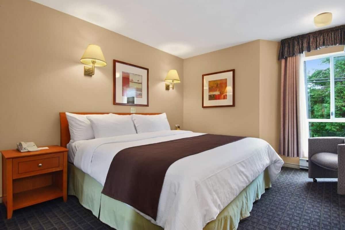 A hotel room with a bed, two bedside lamps, a nightstand, a chair, and a window with curtains.