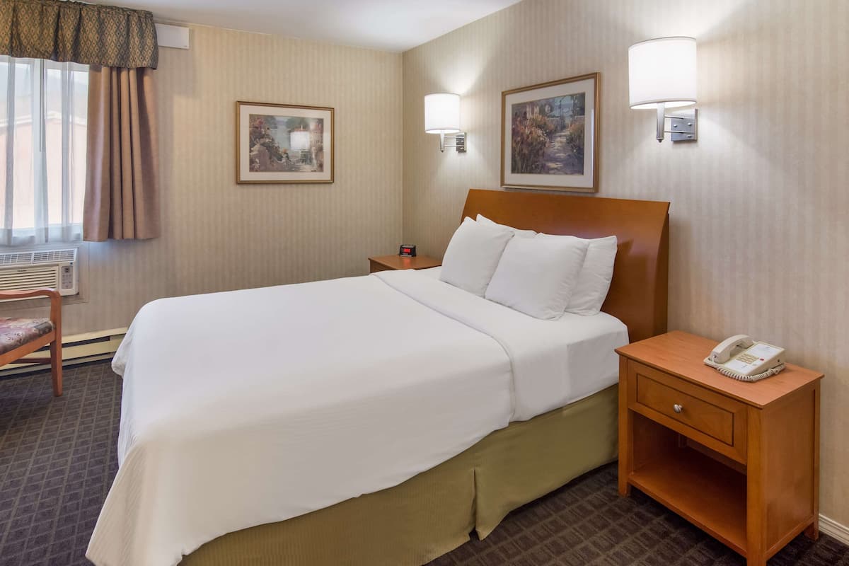 A hotel room with a large bed, a bedside table with a phone, two wall-mounted lamps, and two framed pictures on the wall.
