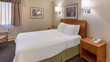 A hotel room with a large bed, a bedside table with a phone, two wall-mounted lamps, and two framed pictures on the wall.