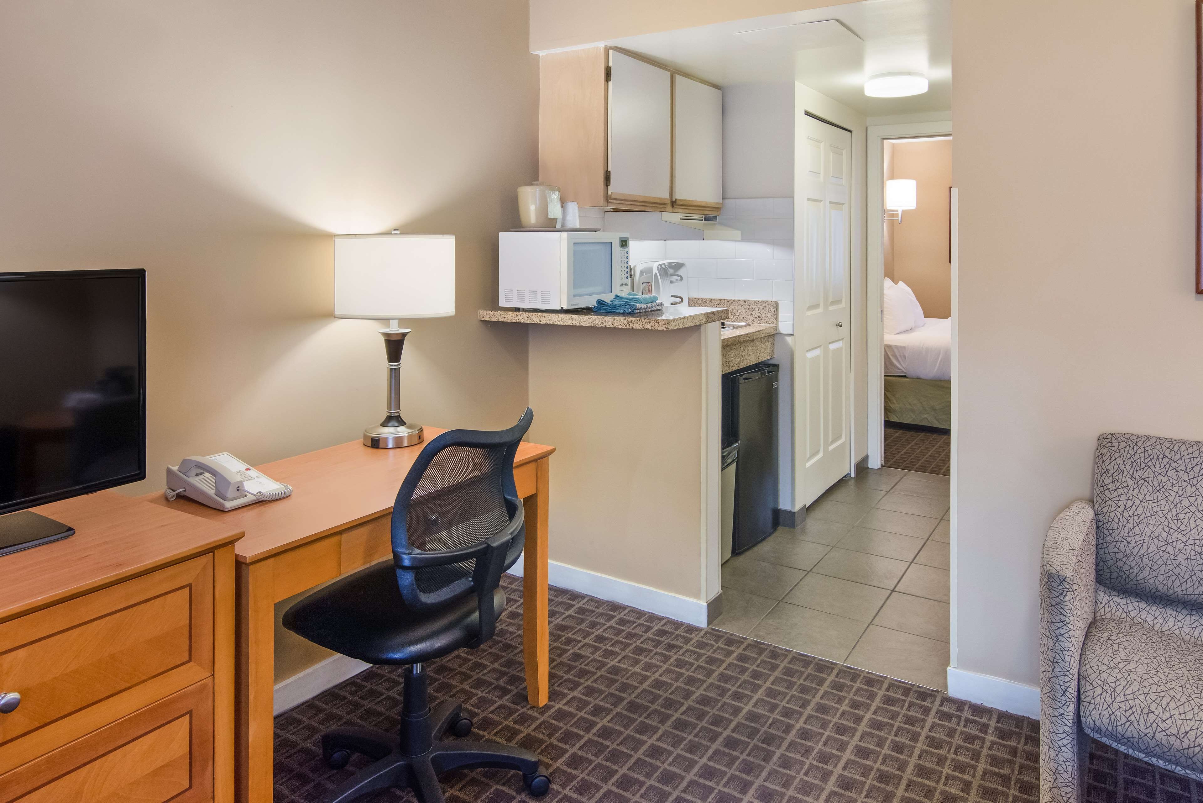 A hotel room with a desk, chair, TV, microwave, and a small kitchenette.