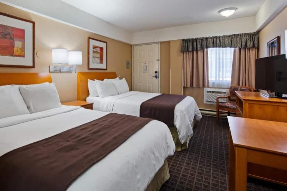 A hotel room with two beds, a desk, a television, and a window with curtains.