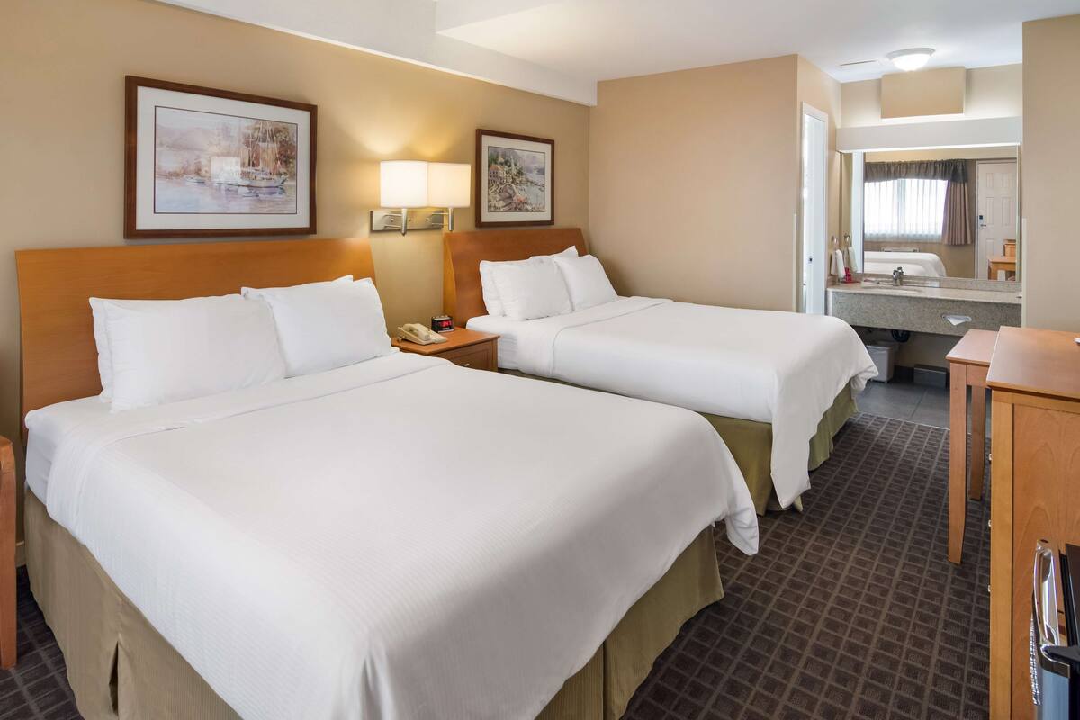 A hotel room with two beds, a bathroom with a mirror, and a small desk.