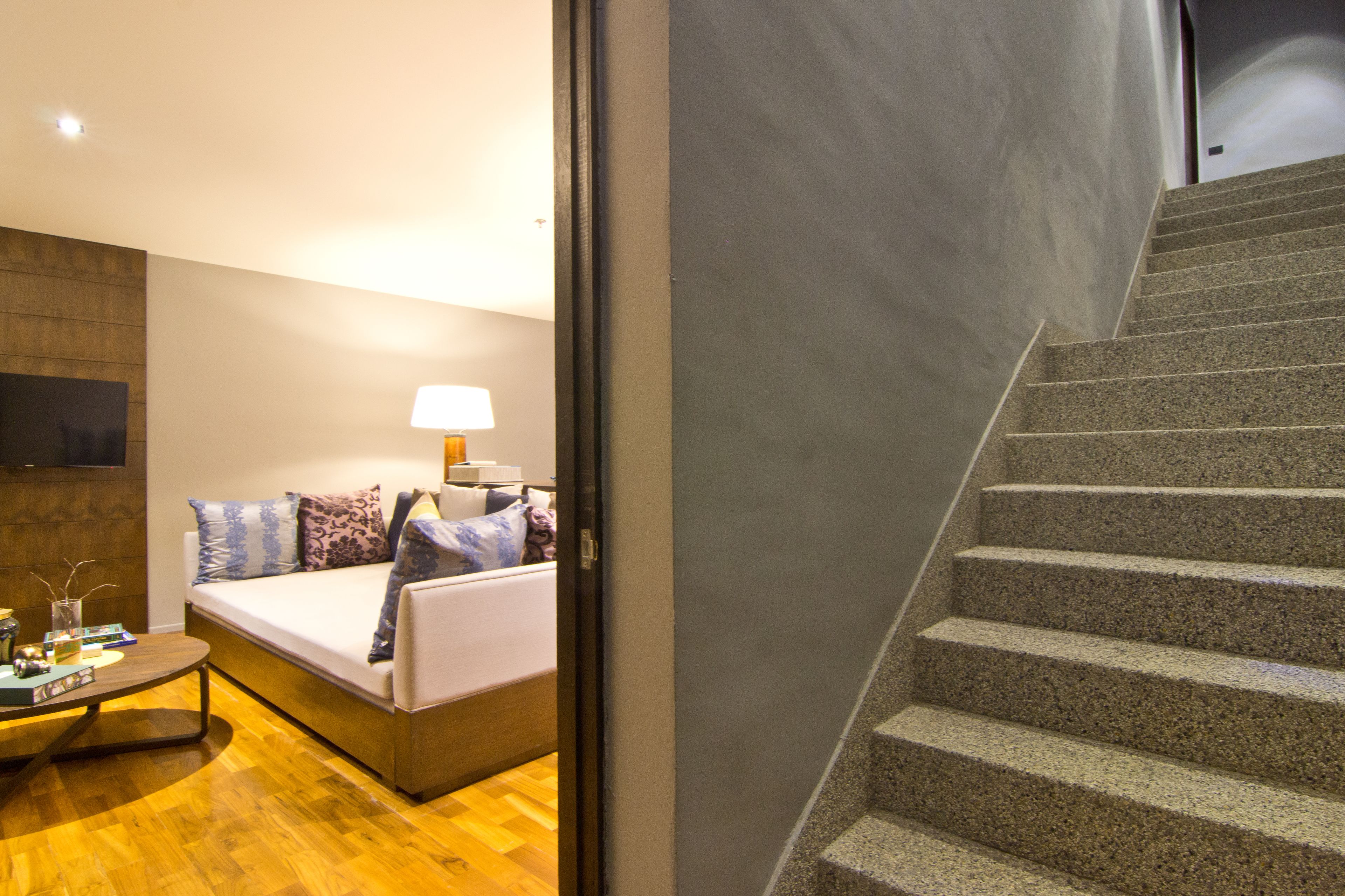 A modern hotel room with a bed, bedside table, lamp, and a view of a staircase.