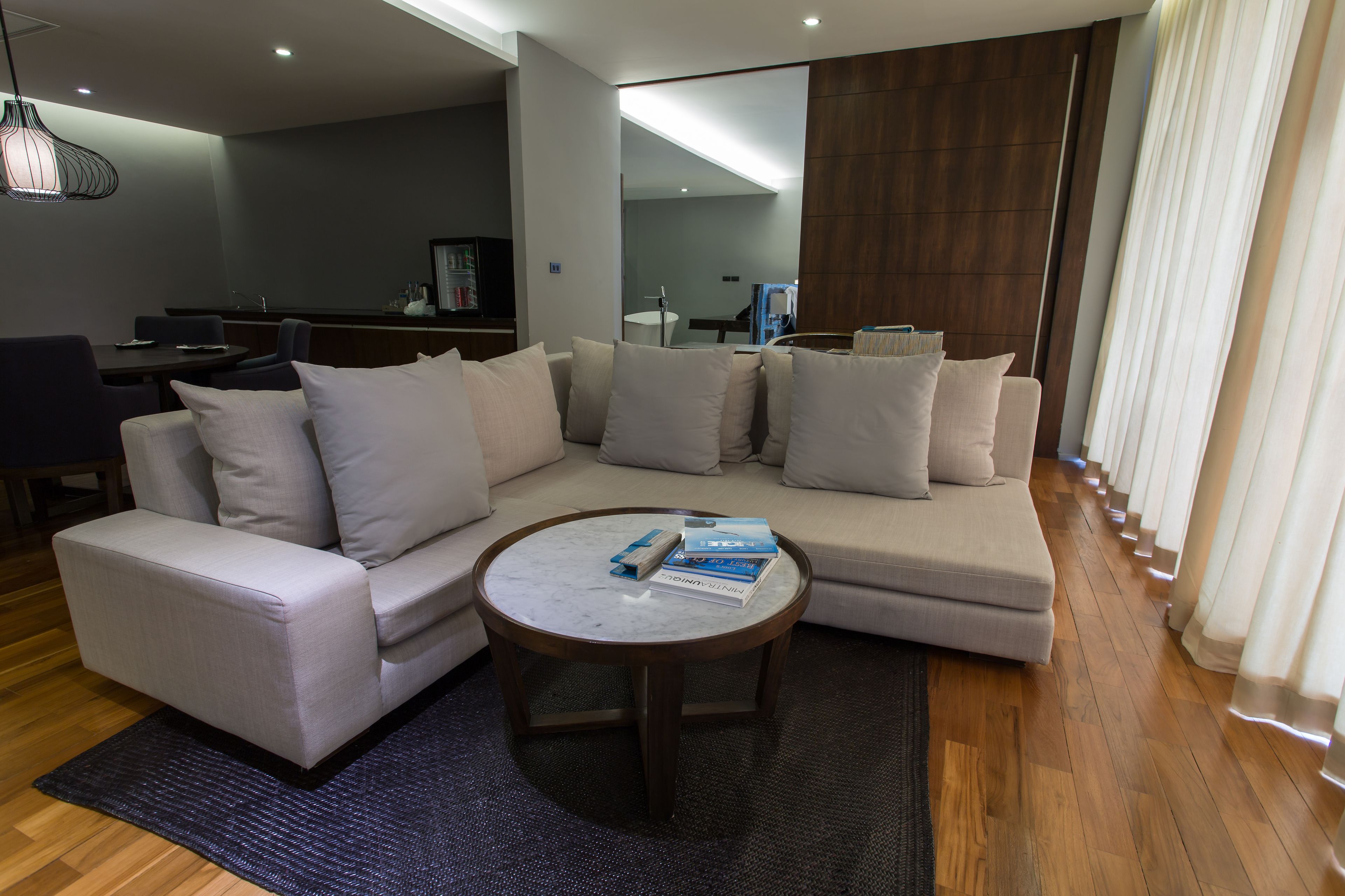 Una sala moderna con un sofá seccional, una mesa de centro redonda y un comedor con una mesa y sillas de madera oscura.