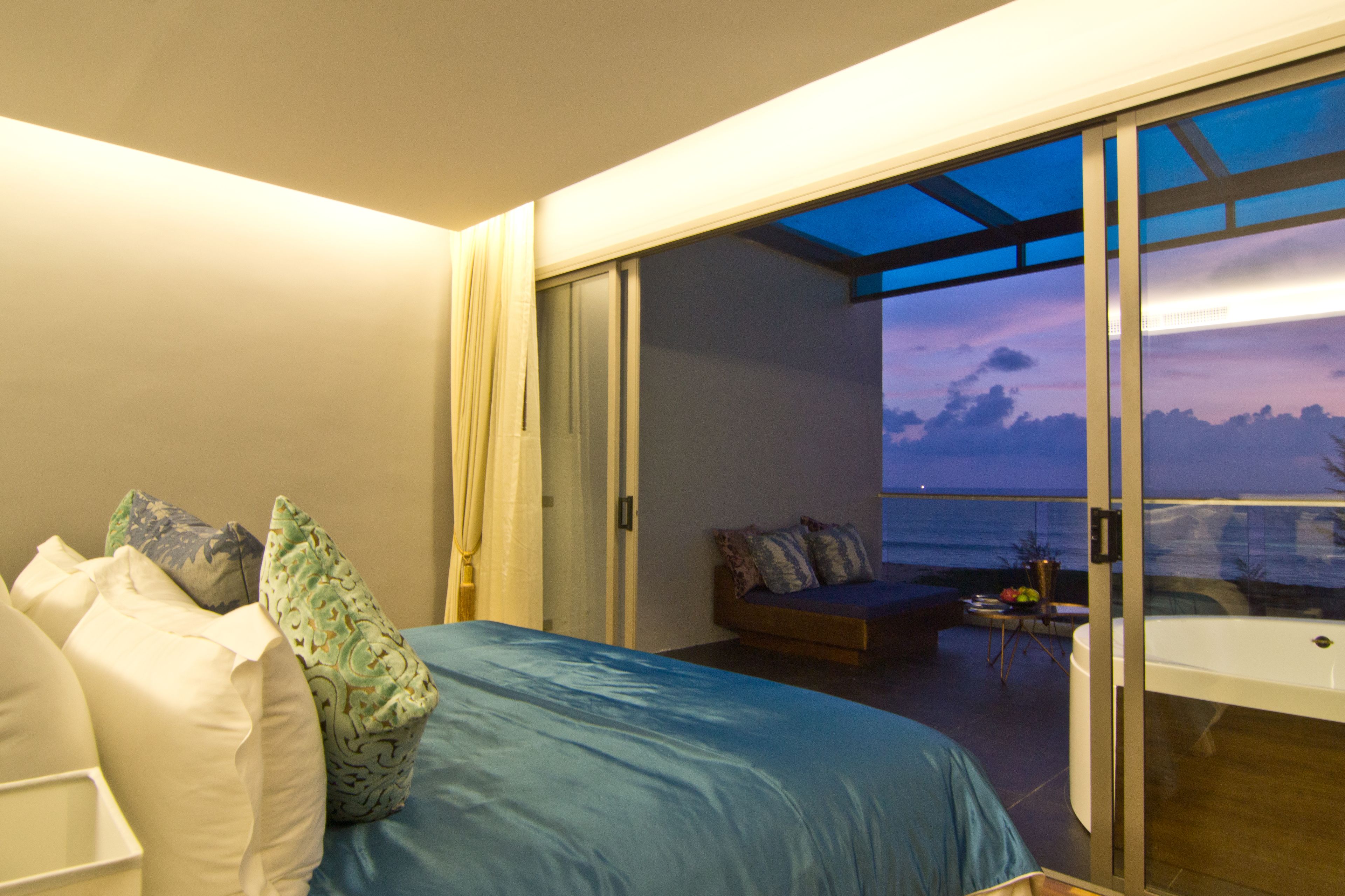 A bedroom with a large bed, a sofa, and a view of the ocean through a sliding glass door.