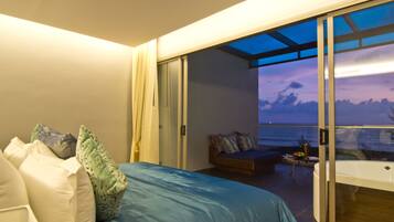 A bedroom with a large bed, a sofa, and a view of the ocean through a sliding glass door.