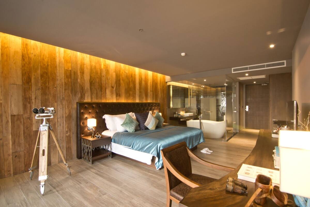 A modern bedroom with a wooden accent wall, a bed with a blue bedspread, a tripod, and a desk with a chair.