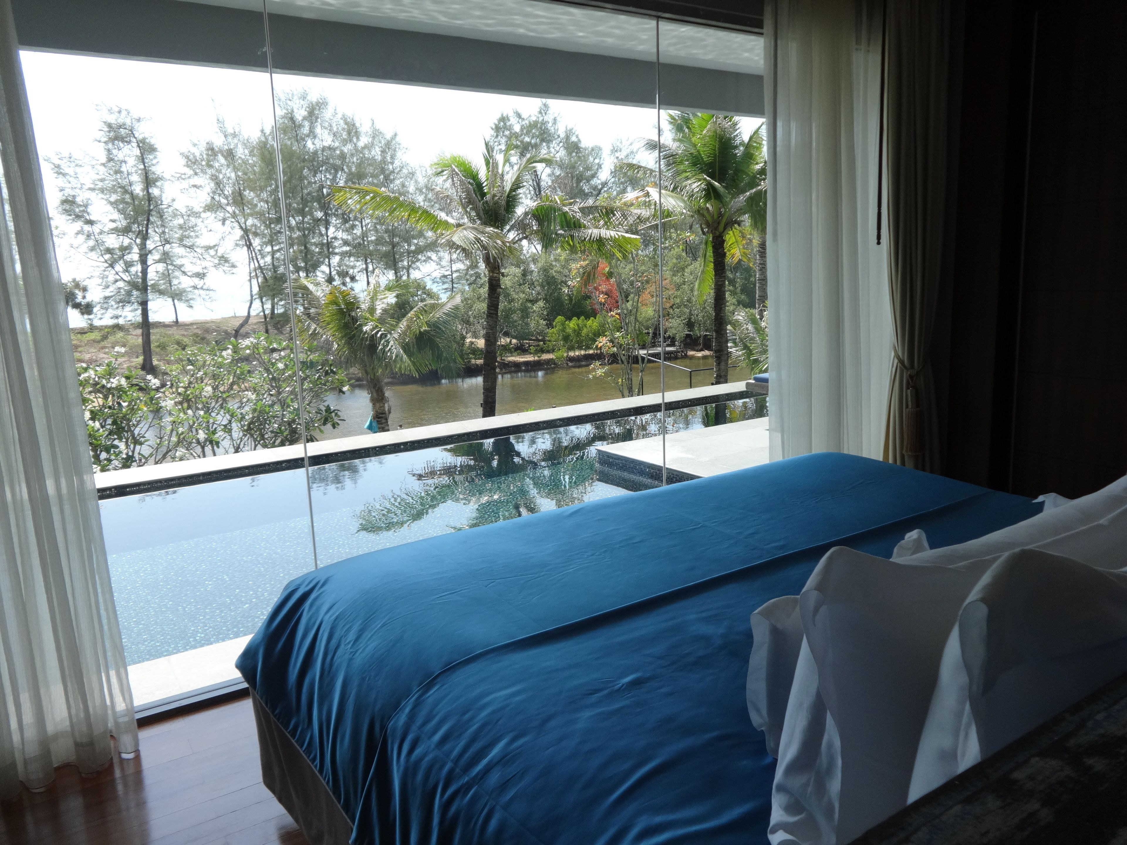Un dormitorio con un ventanal que da a una piscina y follaje tropical.